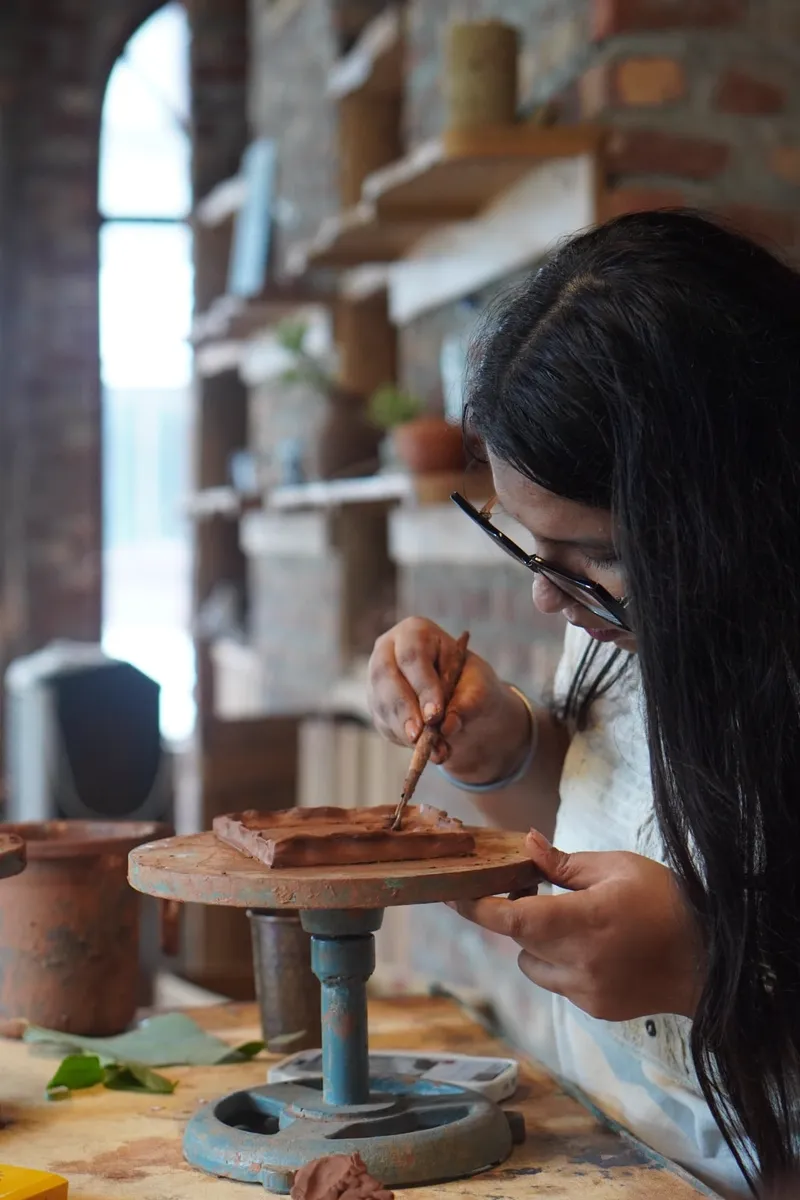 A guest adding surface detail to a clay piece at the studio table at Aavya Pottery & Art Studio
