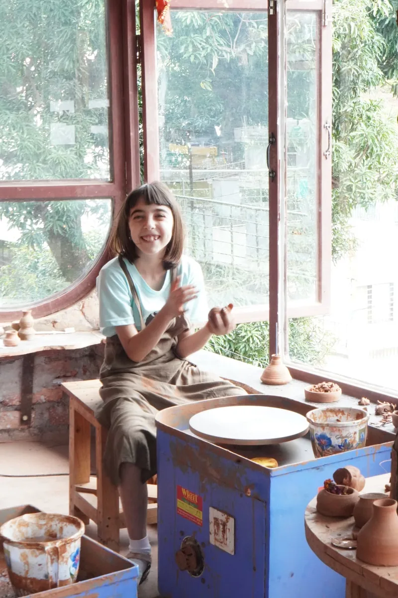 A young guest smiling at the pottery wheel beside the studio windows