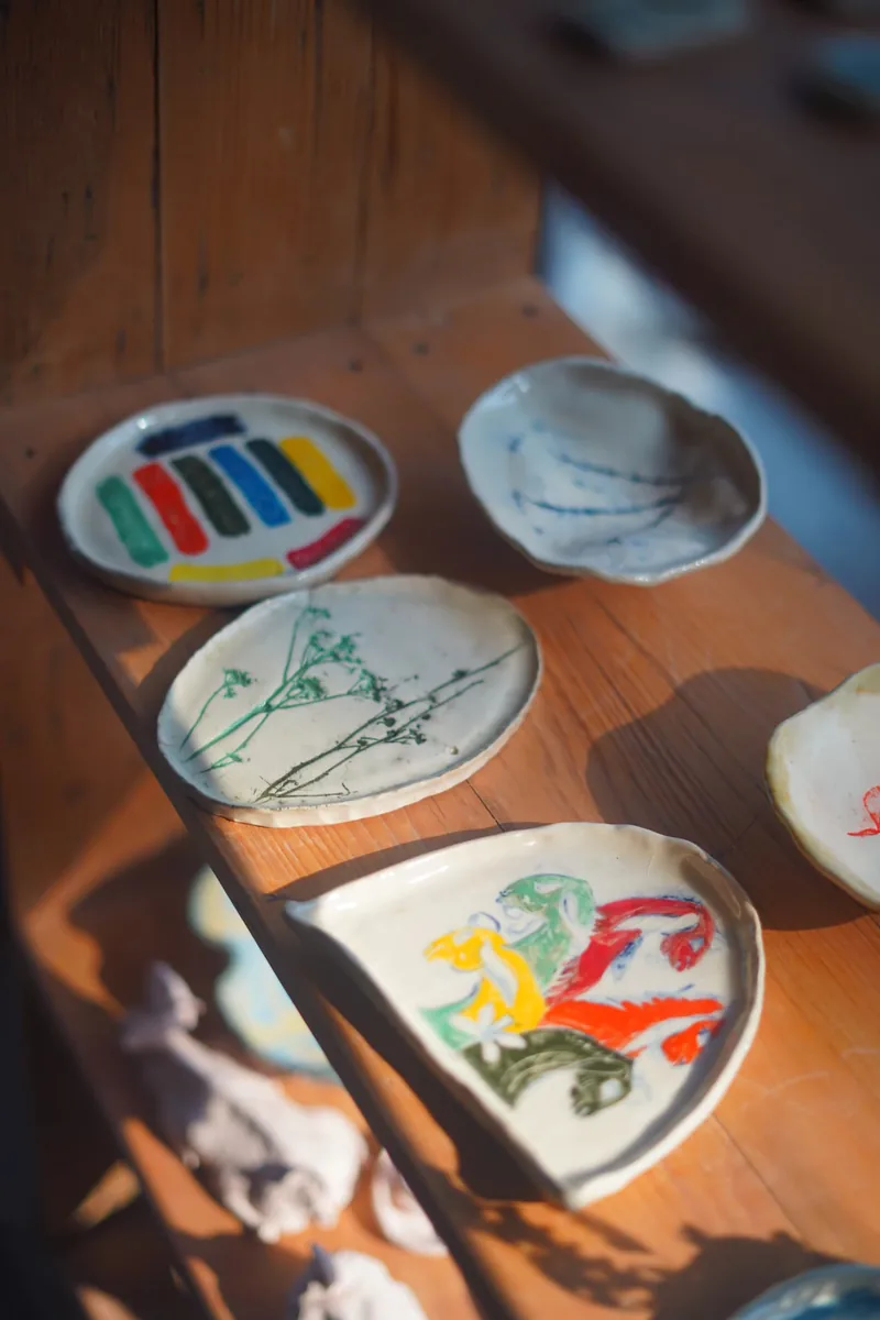 Hand-painted ceramic dishes on a sunlit wooden shelf at the Aavya studio shop