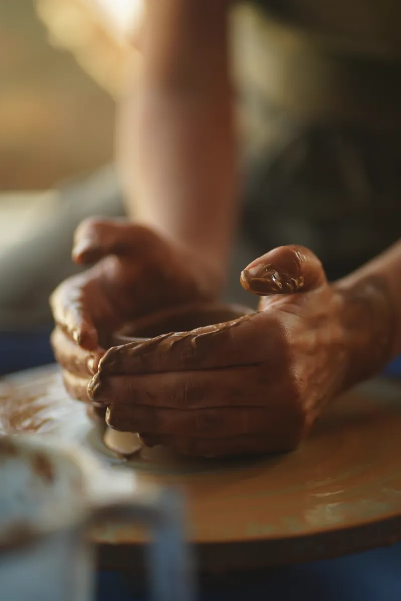 Hands shaping a small clay pot on the wheel in warm studio light at Aavya Pottery & Art Studio