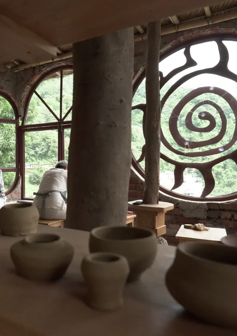 Unfired clay pots on the studio table with a guest at the arched window and the spiral window beyond at Aavya Pottery & Art Studio
