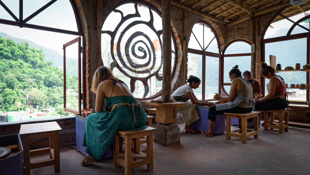 Guests sitting at pottery wheels in the Aavya terrace studio with spiral window and mountain views